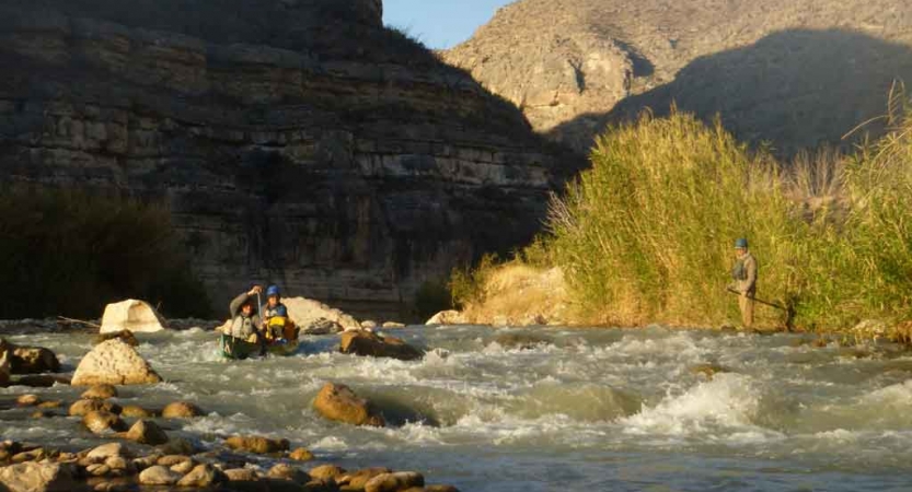 two gap year students paddle a canoe through whitewater while canyon walls rise high in the background